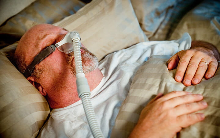 A middle-aged caucasian man sleeping peacefully in bed with his CPAP machine providing therapy for his sleep apnea