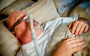 A middle-aged caucasian man sleeping peacefully in bed with his CPAP machine providing therapy for his sleep apnea