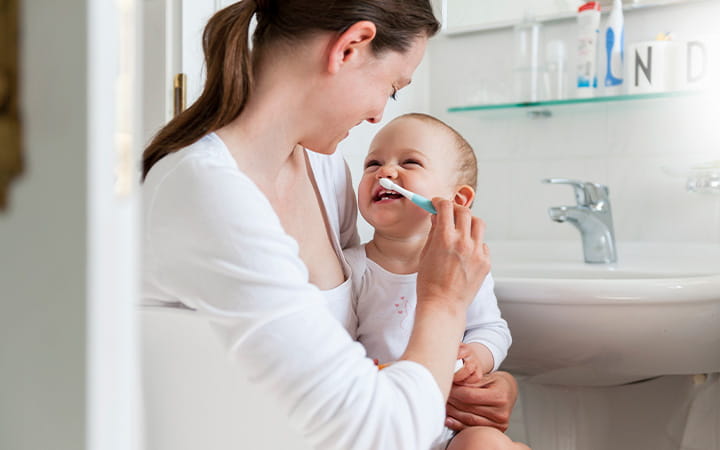 Mother brushing her smiling baby's teeth in bathroom