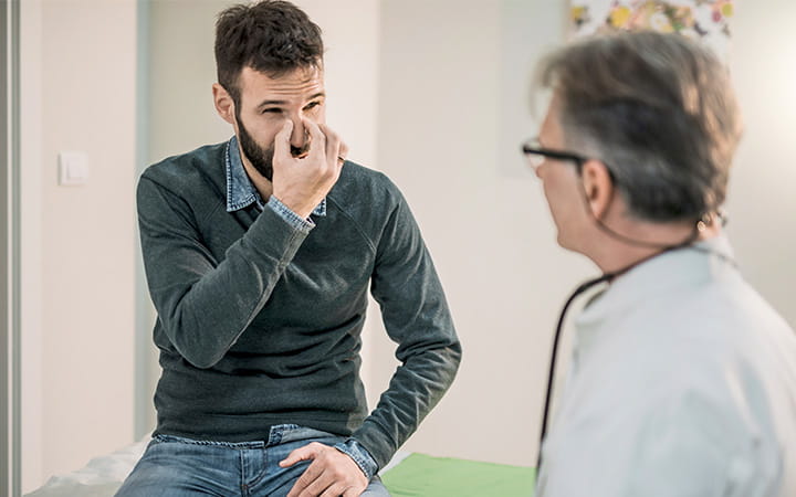man pinching nose and talking with doctor