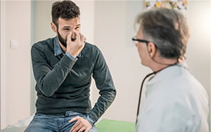 man pinching nose and talking with doctor