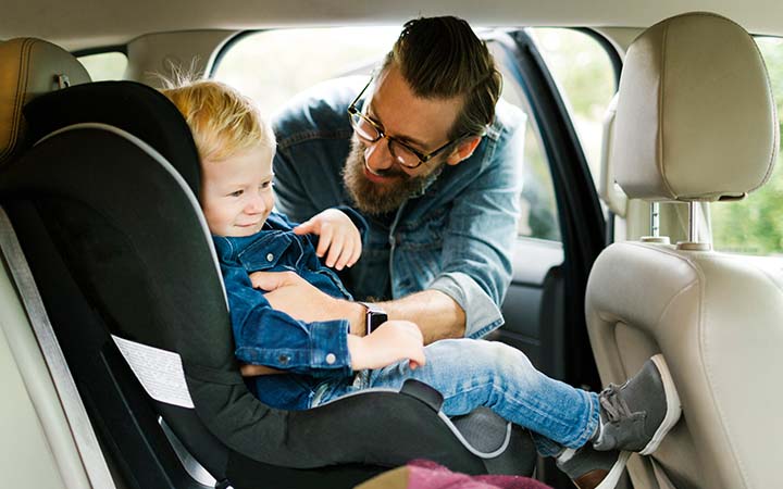 father buckling young child into car seat