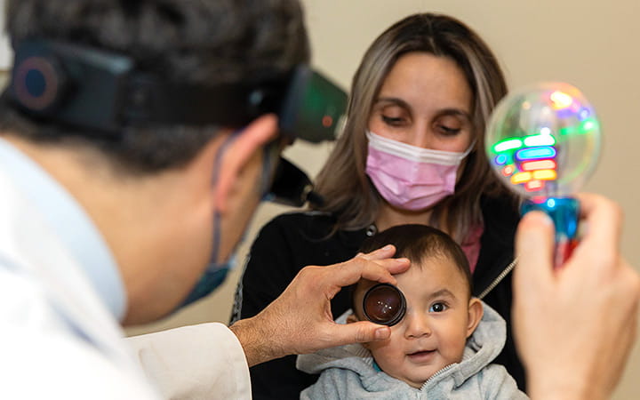 A woman holds her infant son during a pediatric ophthalmology exam