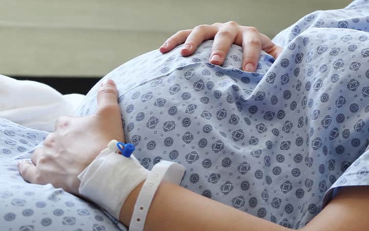 Pregnancy woman in hospital gown holding belly