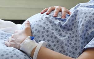 Pregnancy woman in hospital gown holding belly