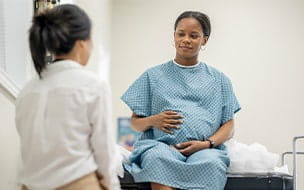 A young pregnant woman sit up on an exam table in her doctor's office during a routine prenatal check-up