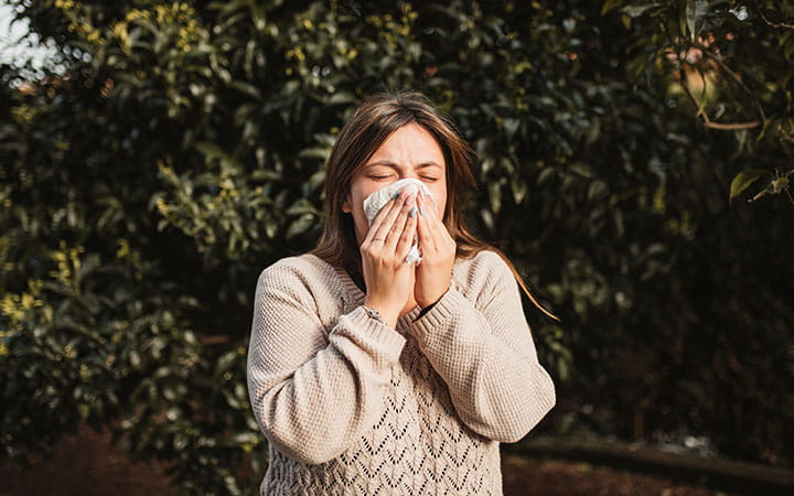 woman sneezing into tissue outdoors