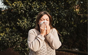 woman sneezing into tissue outdoors