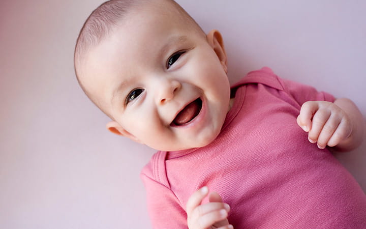 smiling baby lying on its back wearing a light red onesie