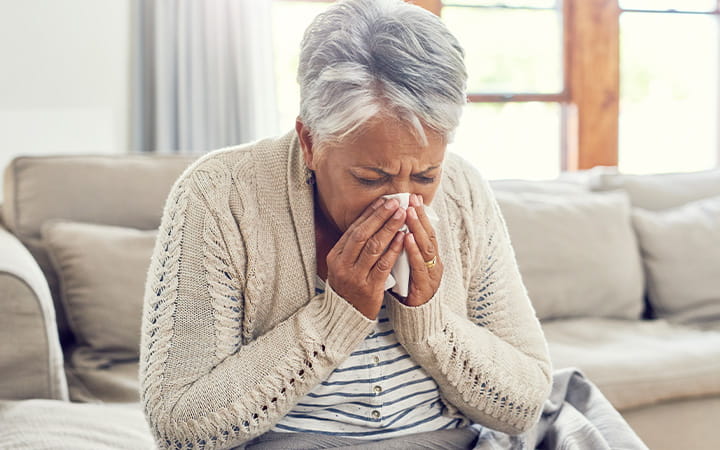 A senior woman sneezes into a tissue