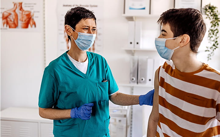 masked female physician with gloved hand on the arm of young teen boy