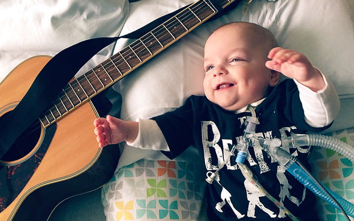 Ryver smiling on a bed next to his father's guitar
