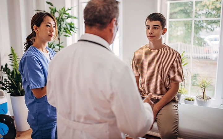 Teen boy talks with doctor and nurse in exam room