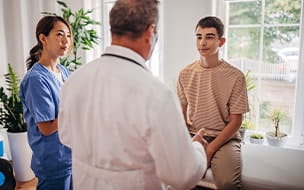 Teen boy talks with doctor and nurse in exam room