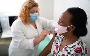 woman in white coat and mask giving older woman a shot