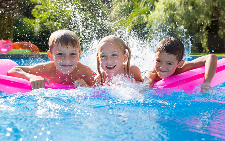 three kids splashing in blue pool with pink inflatable raft