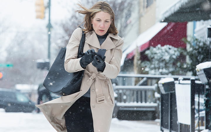 woman walking down snowy street clutching coat