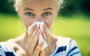 A teenage girl with allergies blowing her nose on a summer day