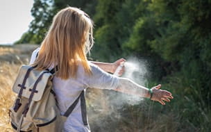 Woman tourist applying mosquito repellent on hand during hike in nature
