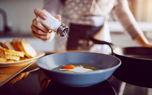 Woman sprinkling salt on an egg cooking in a frying pan.