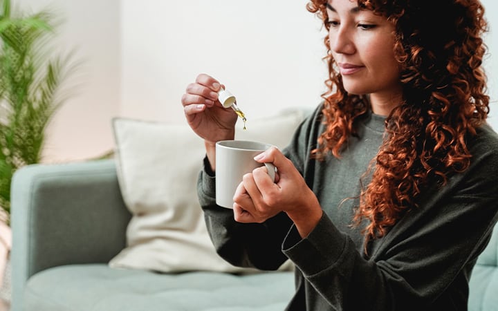 Woman adding CBD oil to her hot drink