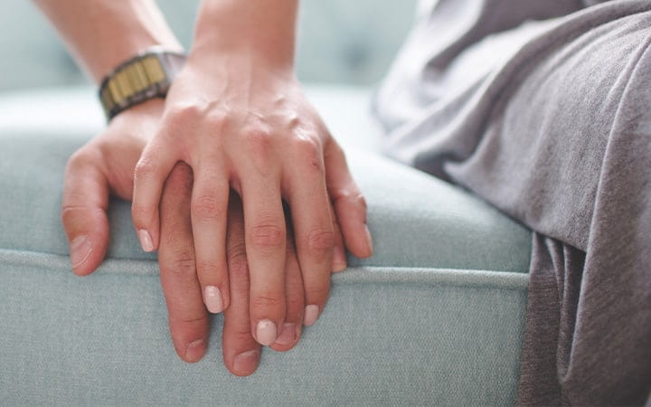 A man and woman holding hands while sitting on a couch
