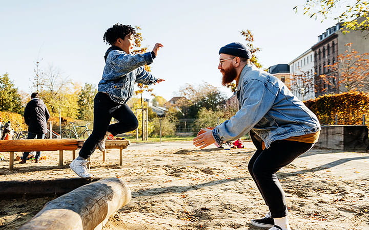 A young boy leaping into his father's arms from a log while messing around in a playground at the park