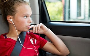 A young girl listening to music on smart phone while looking out the window of a car