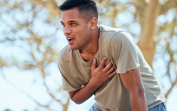 A male athlete holds his chest in pain while running outdoors