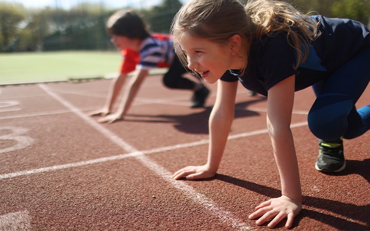 A young girl and boy ready to race on an athletics track