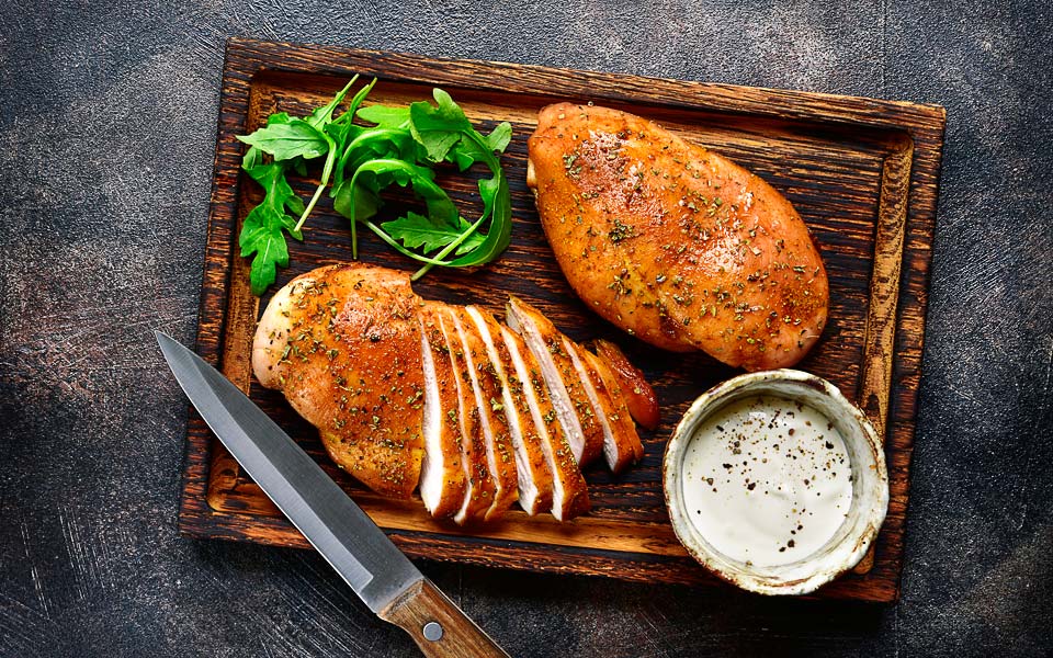 Grilled chicken breast in a sweet and sour marinade with yogurt sauce on a wooden cutting board