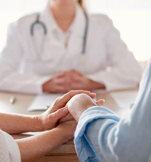 Getty image of couple holding hands talk to doctor regarding infertility issues