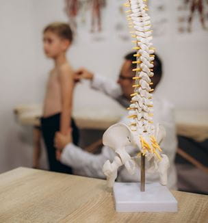 Getty image of patient and doctor in background with pediatric spine skeleton in foreground