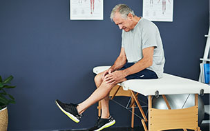 Senior man holding his knee while sitting on the bed in a physiotherapy office