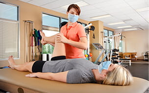 Physical therapist wearing protective face mask evaluates range of motion on female patient