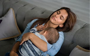 Exhausted mother sleeping in the sofa whole holding her baby