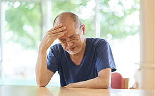 Elderly man sitting at kitchen table holding his head