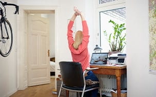 Woman sitting at desk in her home office stretching