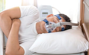 Man sleeping in bed wearing CPAP mask for sleep apnea therapy