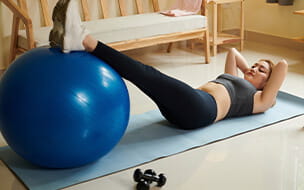 Young woman doing crunches with legs on fitness ball when exercising at home