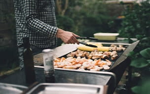 Man grilling prawns, meat and vegetables on barbecue in backyard