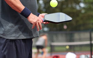 A man holding a pickleball paddle and ball