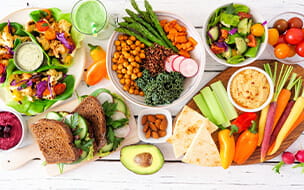 Overhead view of a healthy lunch table scene with nutritious lettuce wraps, Buddha bowl, vegetables, sandwiches, and salad.