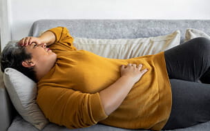 Middle aged woman lying on couch holding stomach in pain.