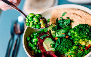 Eating vegan bowl with edamame beans, broccoli, avocado, beetroot, hummus and nuts
