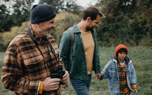 Small boy with father and grandfather walking in forest exploring nature together.