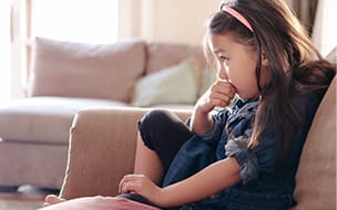 Child with anxiety sitting on the couch biting her finger nails.