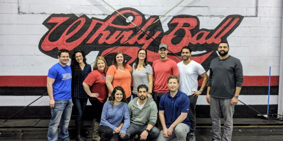 Group of people standing and kneeling in front of Whirly Ball sign