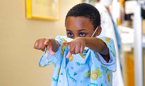 Young african american boy in hospital gown pointing at the camera with both hands