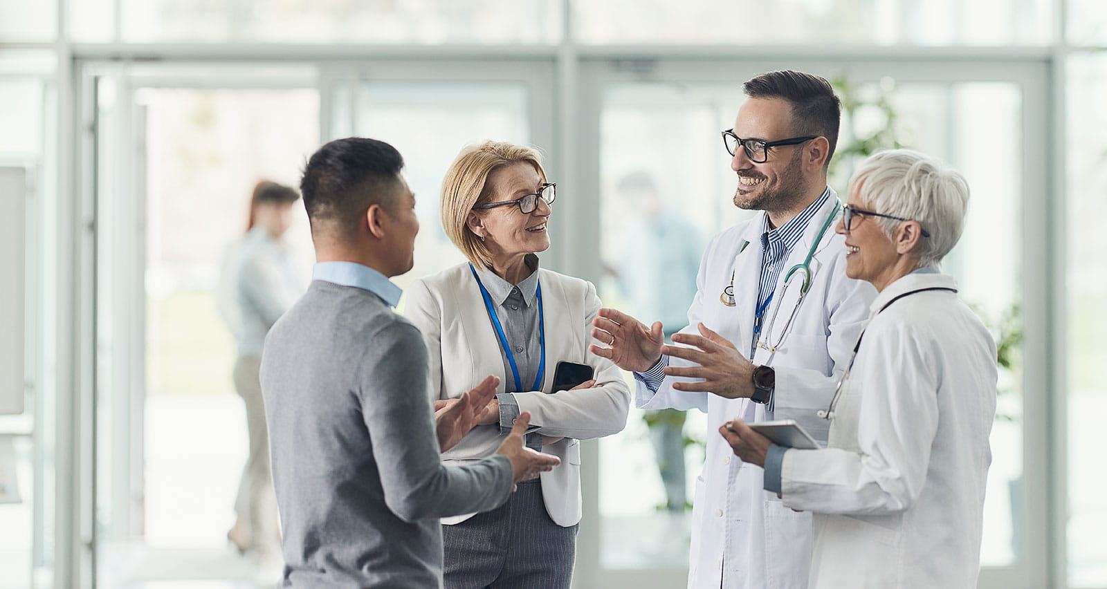 A pari of smiling medical experts communicating with two executives in a the lobby of a medical facility